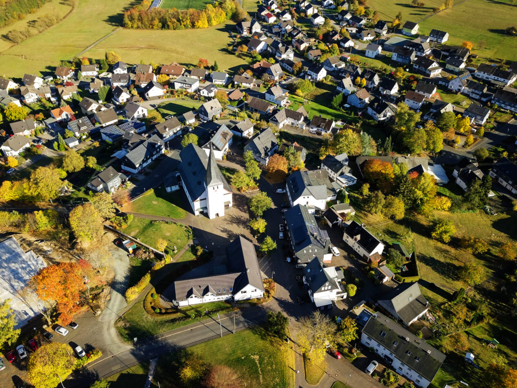 Die Stadt Netphen aus der Luftansicht: Häuser und Kirchturm umringt von grüner Natur